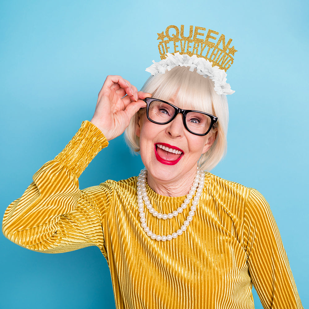 Older woman wearing Gold and white party crown headband that says Queen of Everything