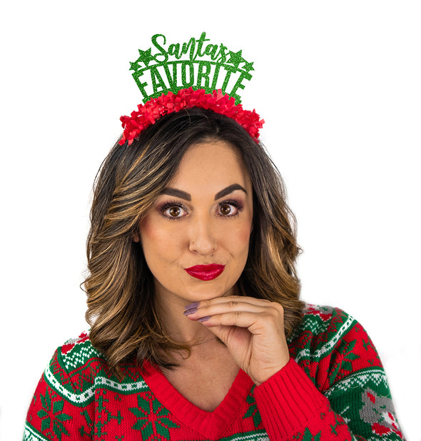 Girl wearing Christmas sweater and Green glitter and red fringe party crown that says "Santa's Favorite" "Santa's" is in cursive